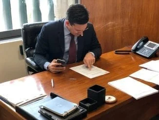 João Roma em uma mesa lendo um documento